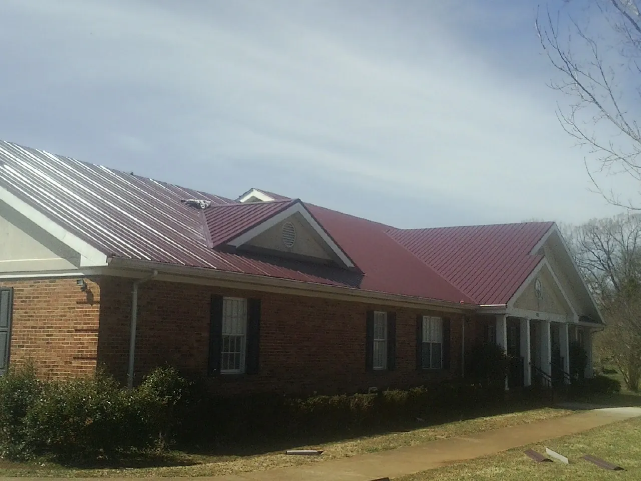 Red metal roof with gabled entries on a long brick building, from a Hail Damage Roof Repair job in Jamesville