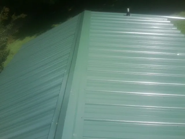 New green metal panels meeting at the ridge of a roof — Flat Roof Repair work by our crew in Jamesville
