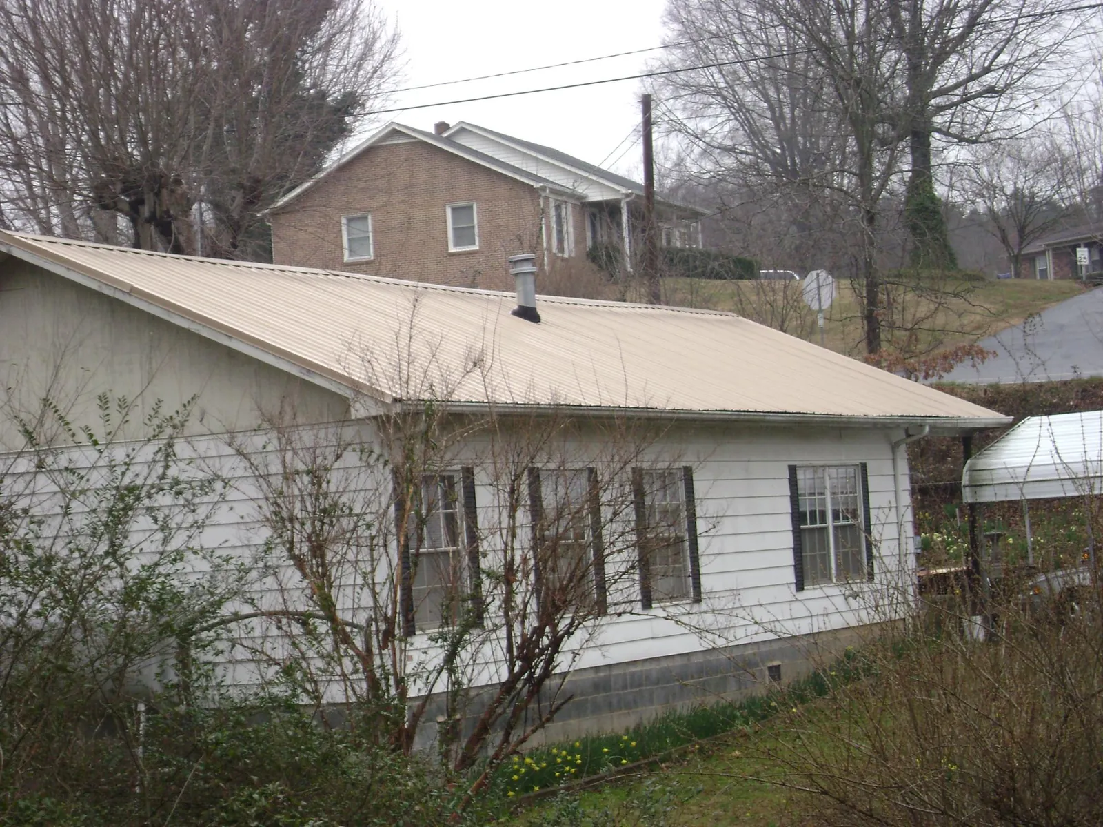 Tan metal roof on a white sided house set into a hillside — Commercial Roofing by Roofing Brothers in Jamesville