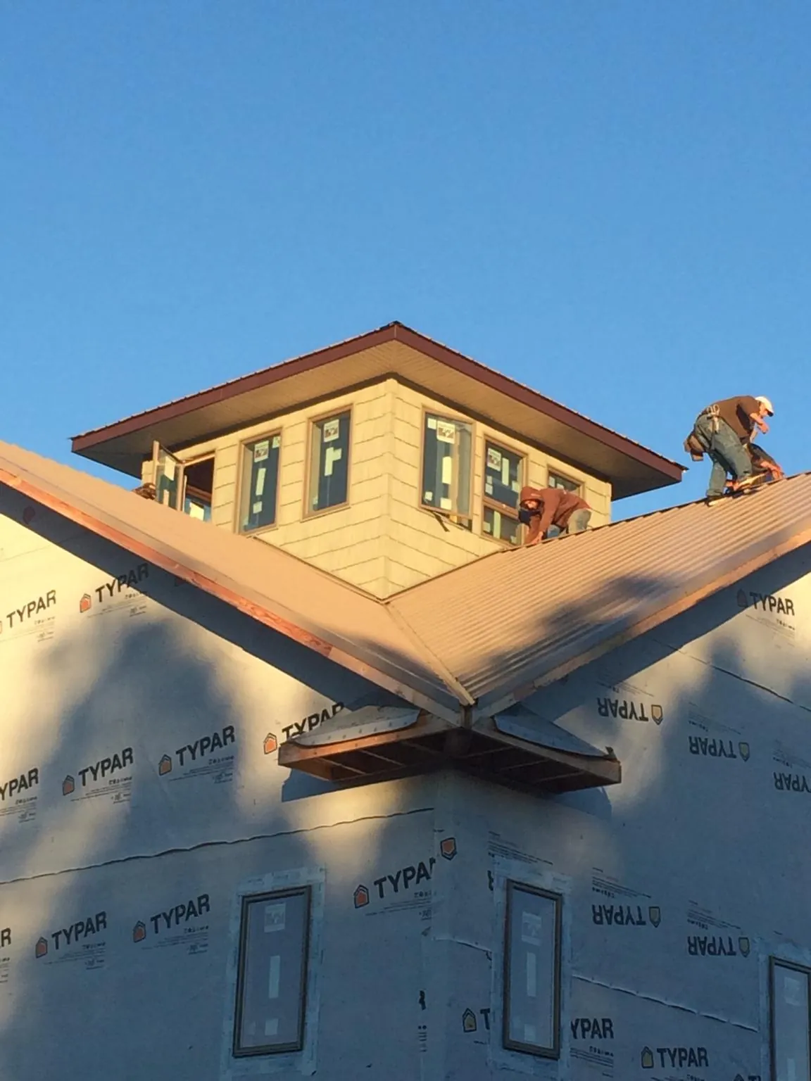 Roofers working around a rooftop cupola on a new metal roof at sunset — Roof Waterproofing in Jamesville by Roofing Brothers